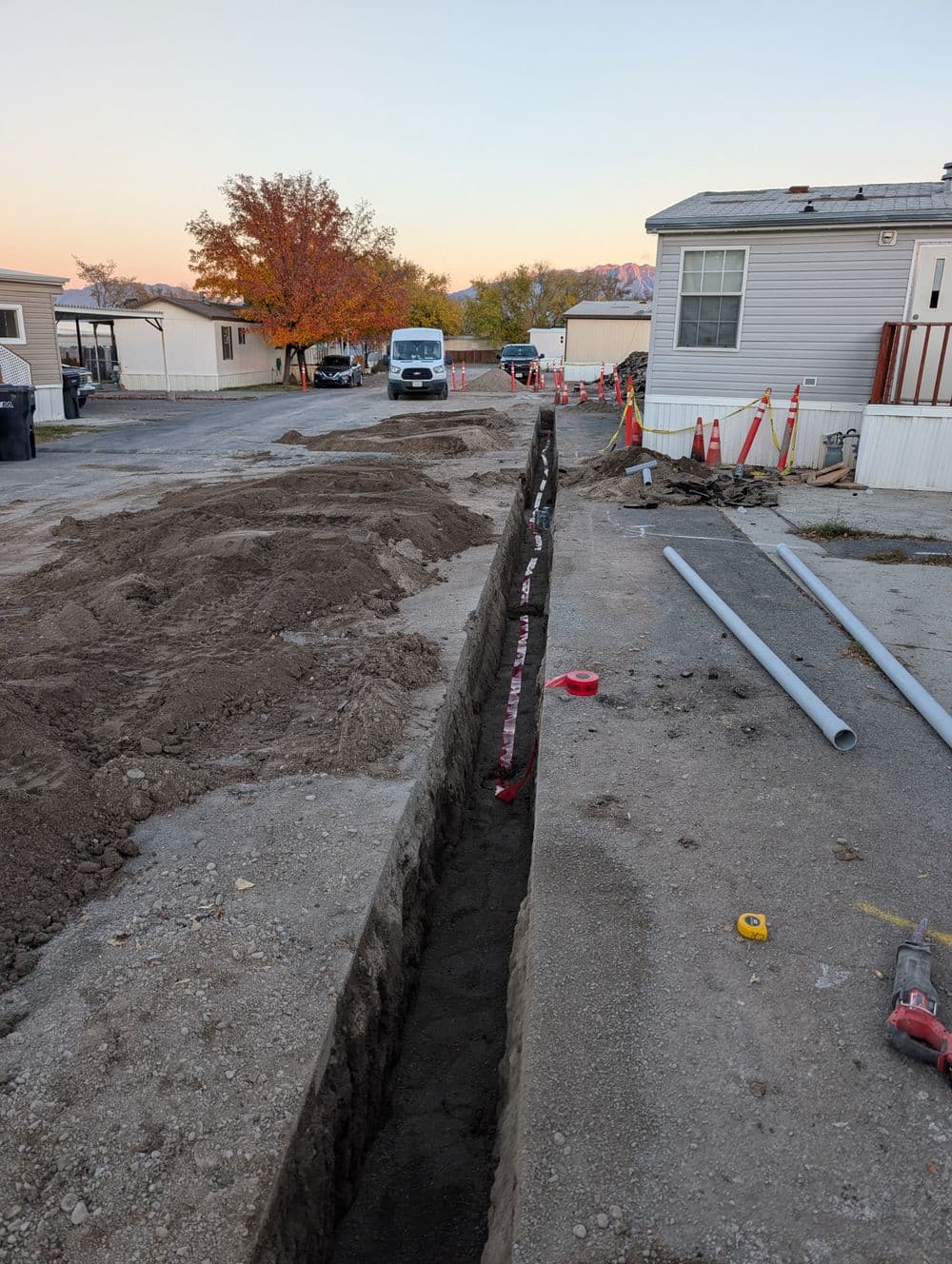 Excavated trench for utility installation in mobile home park with nearby construction materials.
