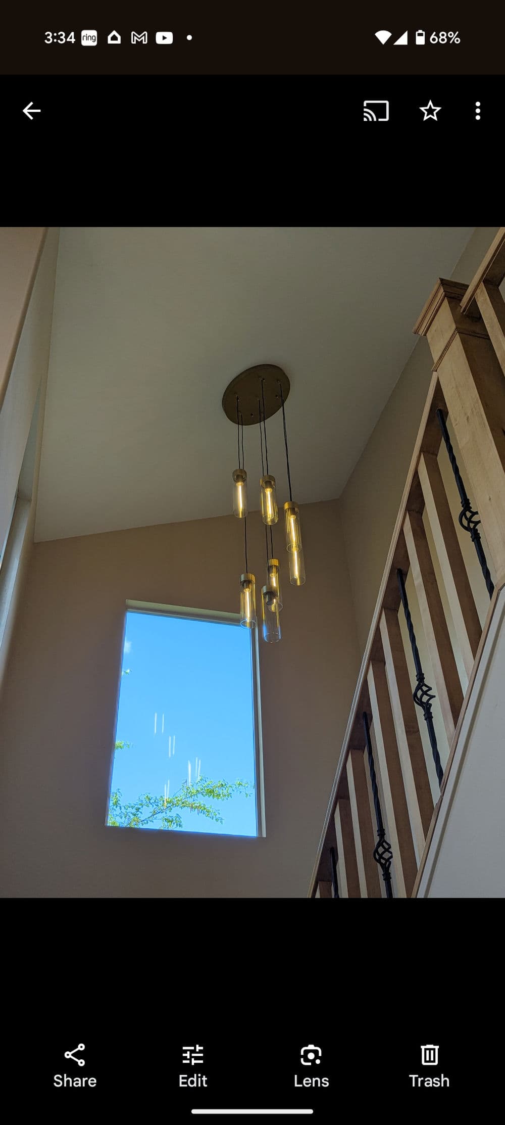 Modern pendant light fixture hanging above a staircase with a window revealing blue sky.