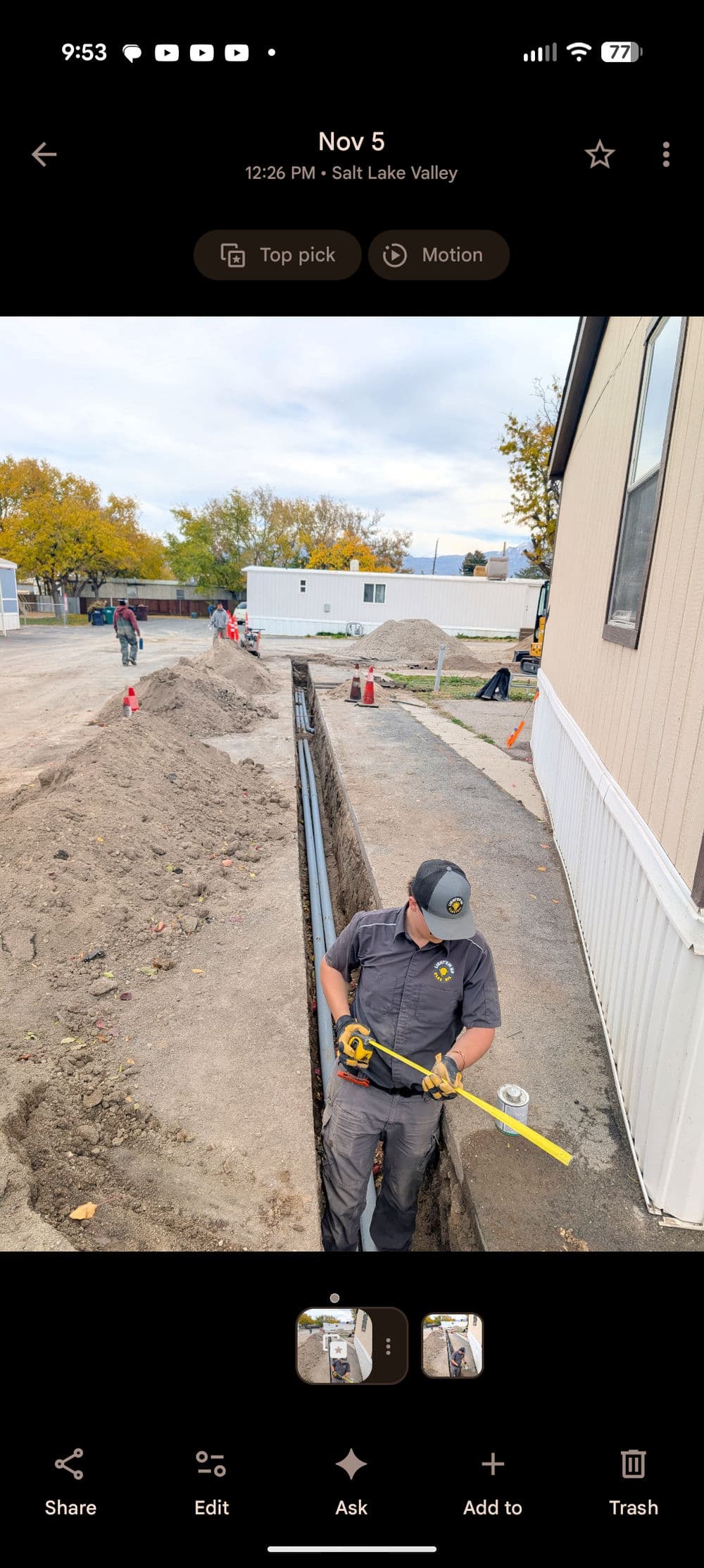 Construction worker measuring trench depth in Salt Lake Valley with team members in background.