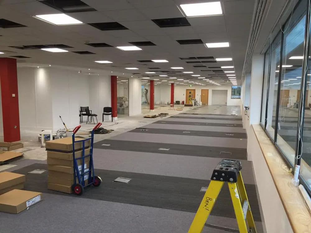 Renovation of a modern office space with carpeting, tools, and furniture in progress.